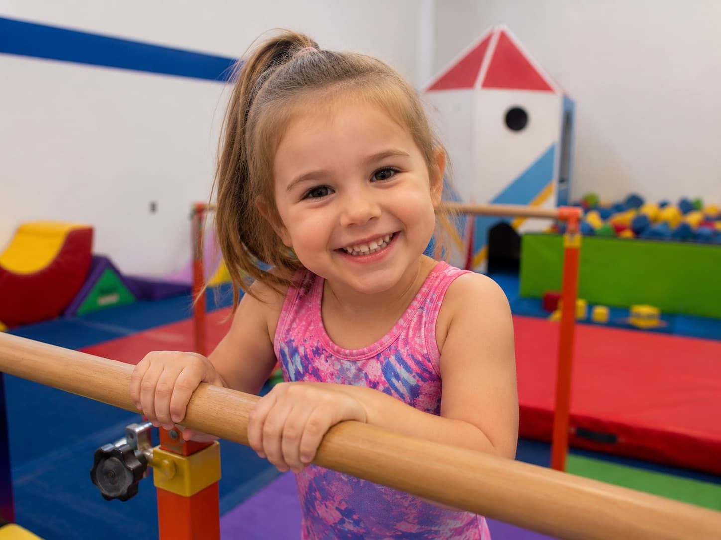 A preschooler smiling while holding the bars at Gym Stars